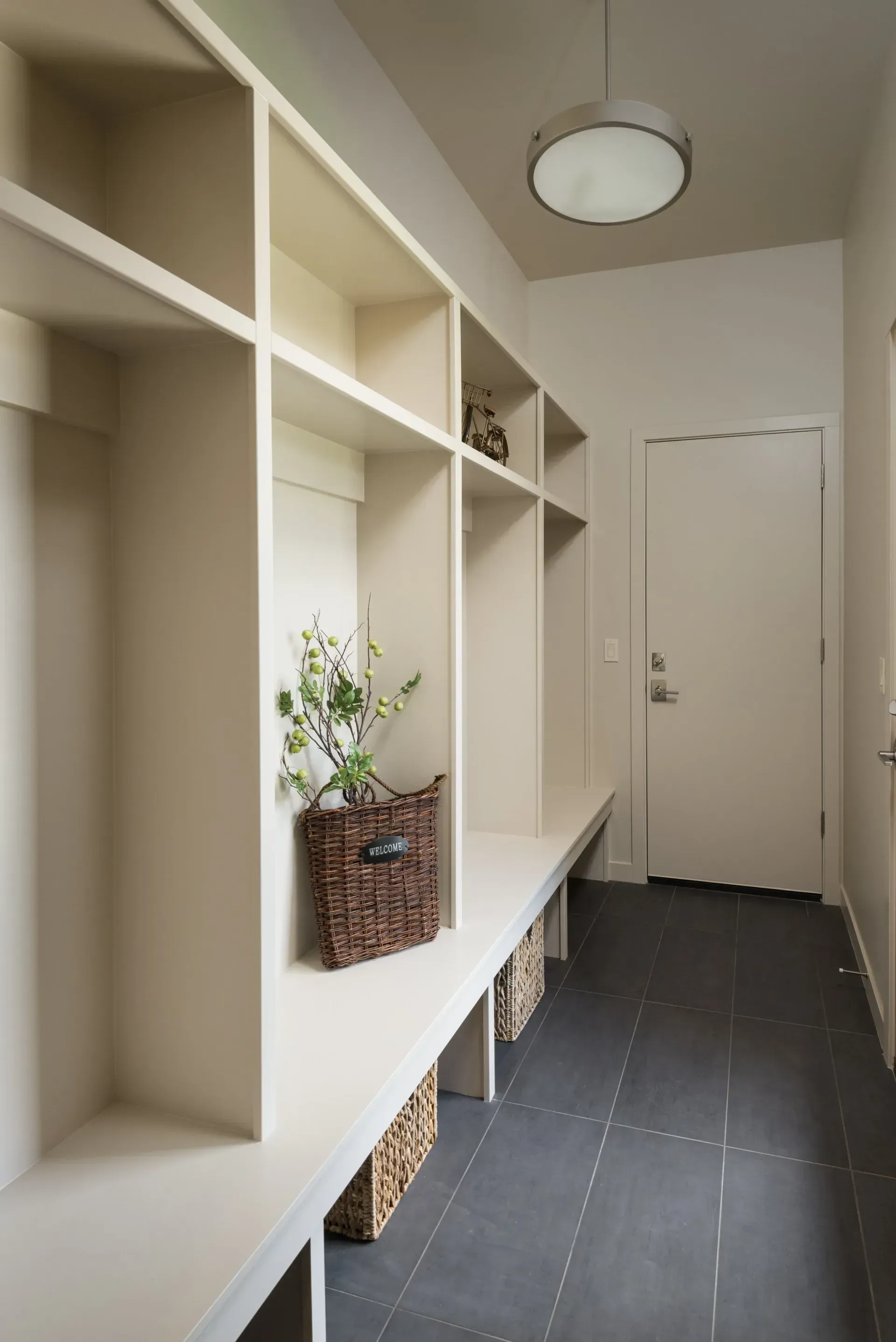 Built-in hallway shelves with wicker baskets and a white door at the end of a narrow corridor