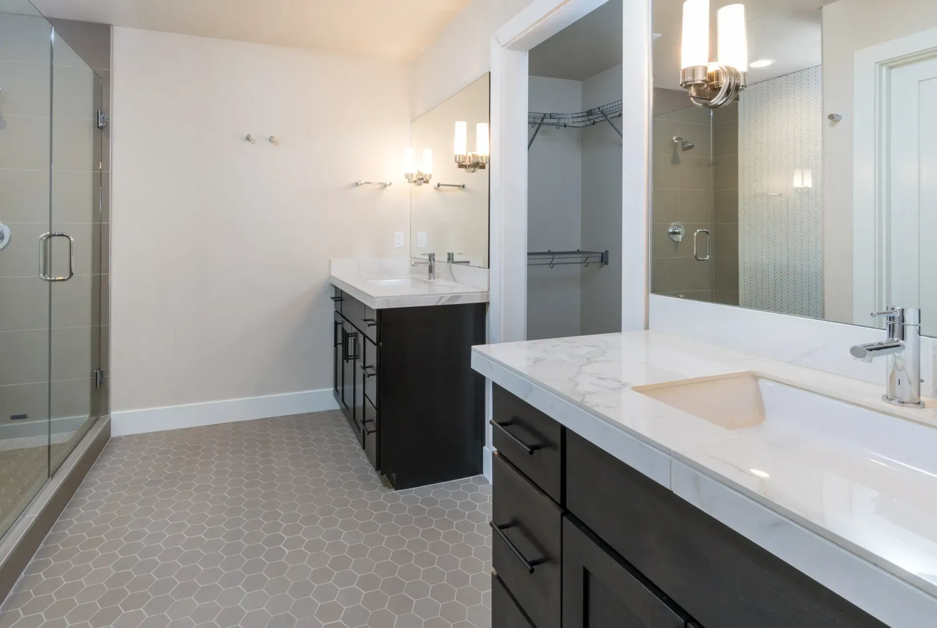 Modern bathroom with double vanity, white countertops, dark cabinets, and glass shower enclosure.
