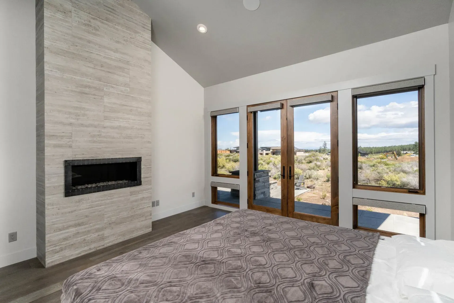 Modern bedroom with large windows, gray carpet, and a fireplace, overlooking a scenic landscape