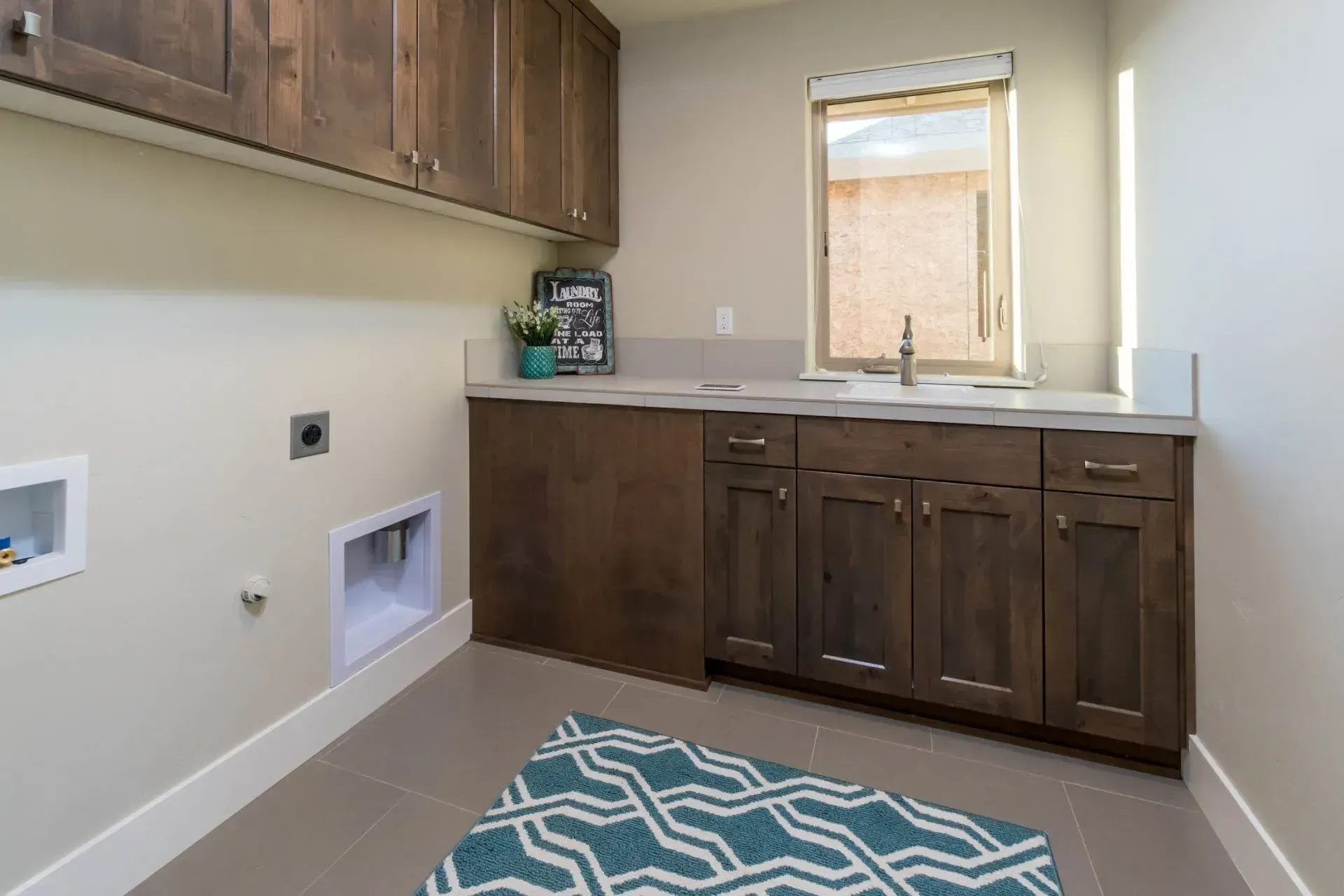 Empty laundry room with brown cabinets, utility hookups, sink, and a blue patterned rug