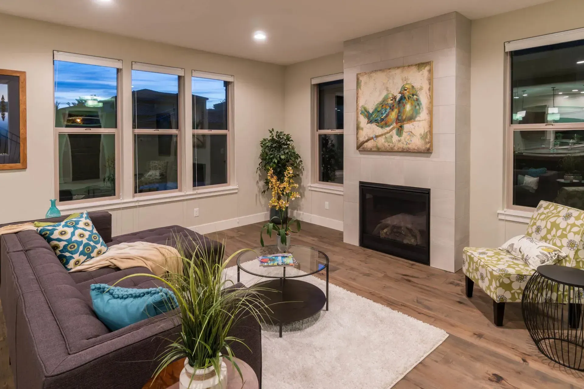 Modern living room with gray sofas, fireplace, coffee table, and large windows at dusk