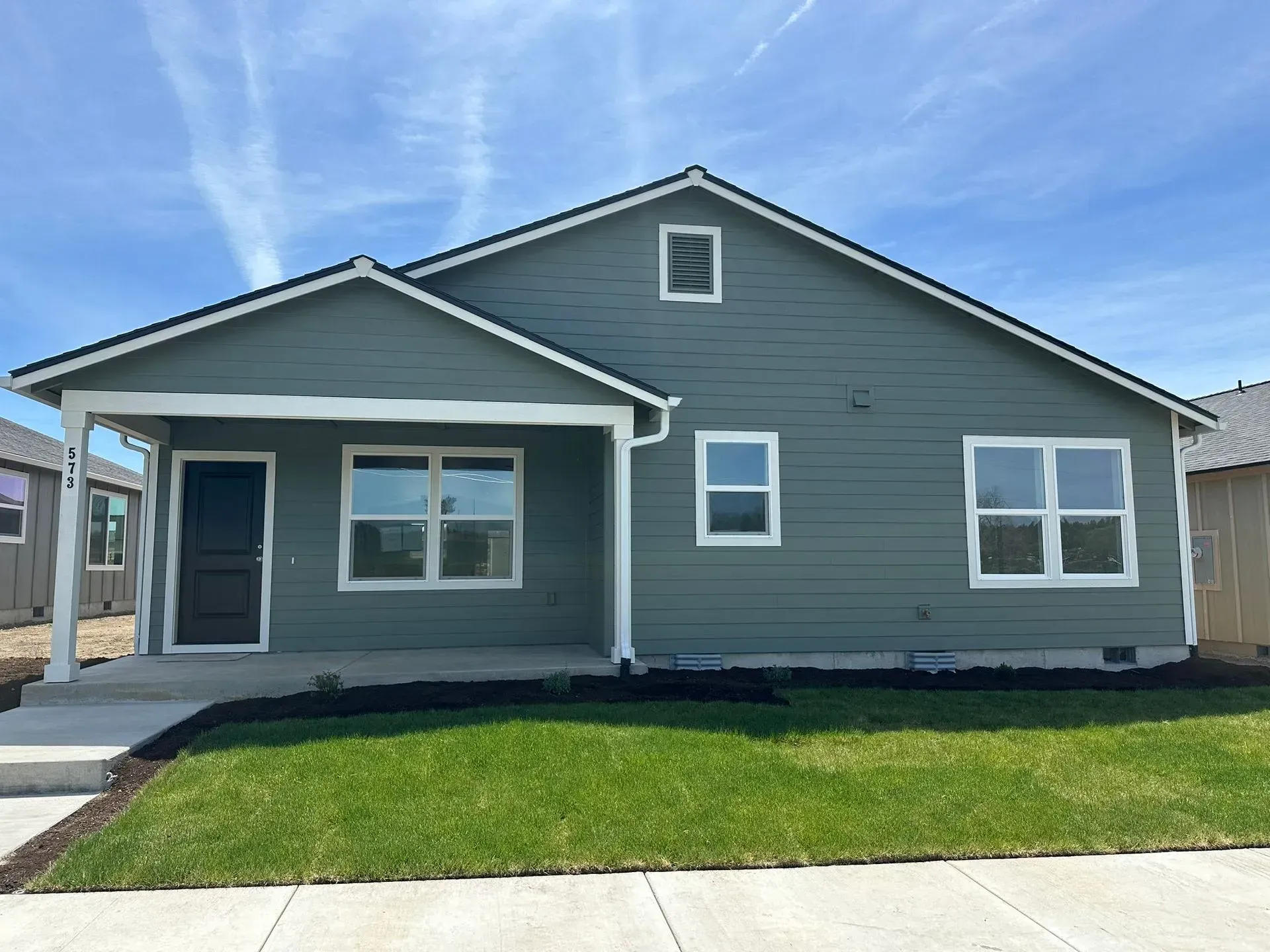 Single-story blue house with white trim, front porch, and green lawn under a clear sky