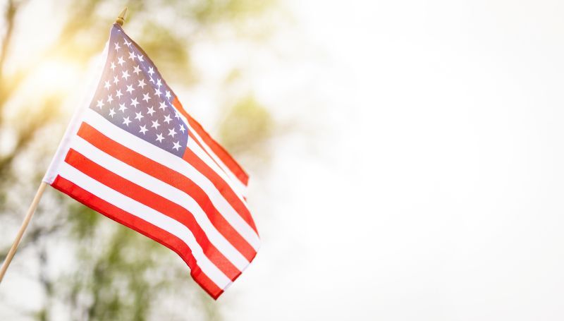 American flag waving on a pole against a bright, blurred outdoor background