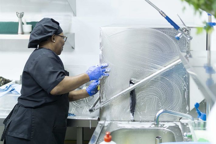 Person washing a large metal tray at a kitchen sink in a commercial kitchen