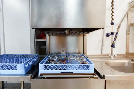 Commercial kitchen sink area with a stainless hood, blue dish racks, and a dishwashing machine