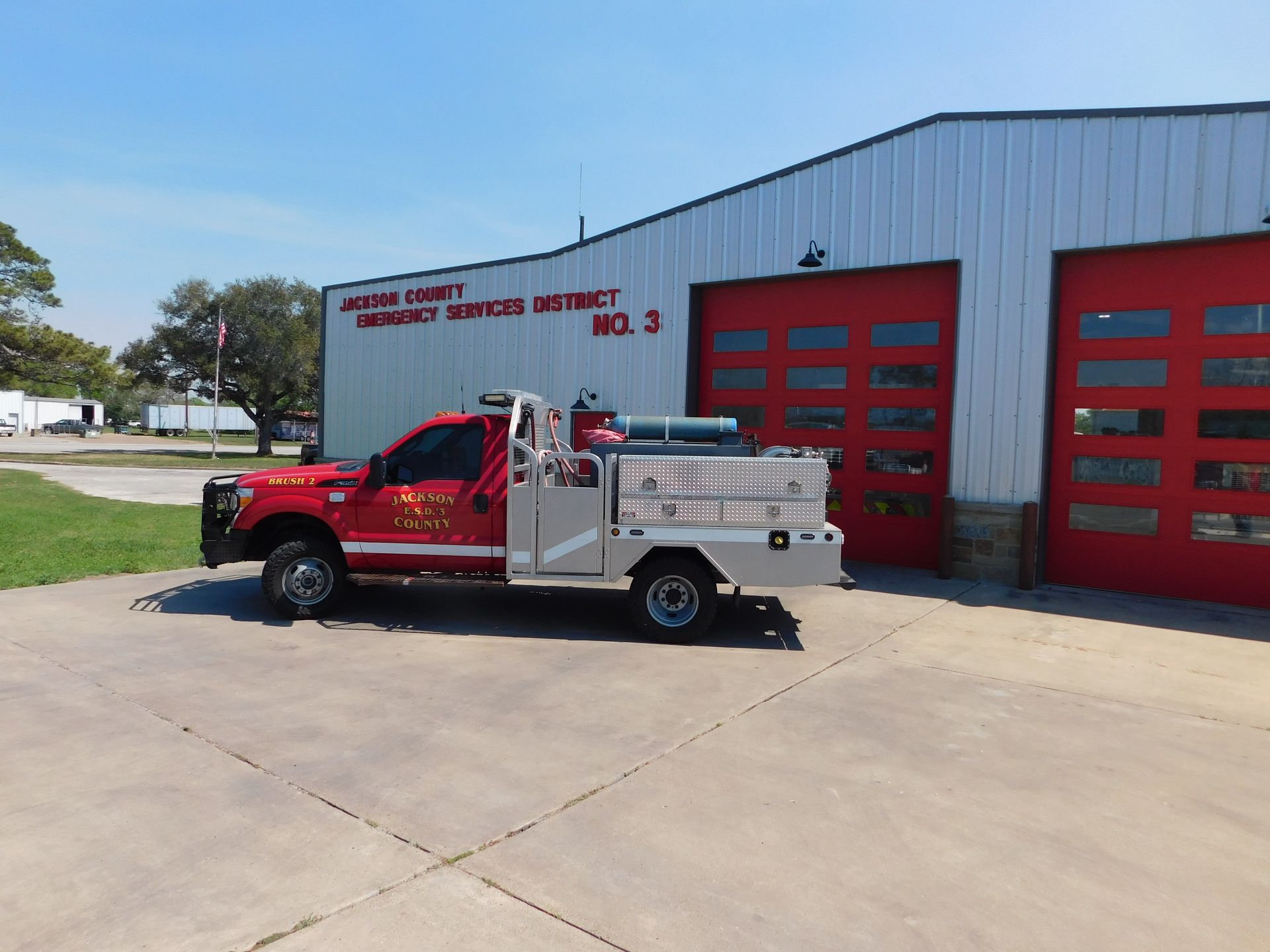 A red Jackson County fire department utility truck parked outdoors on a paved lot under a sunny blue sky.