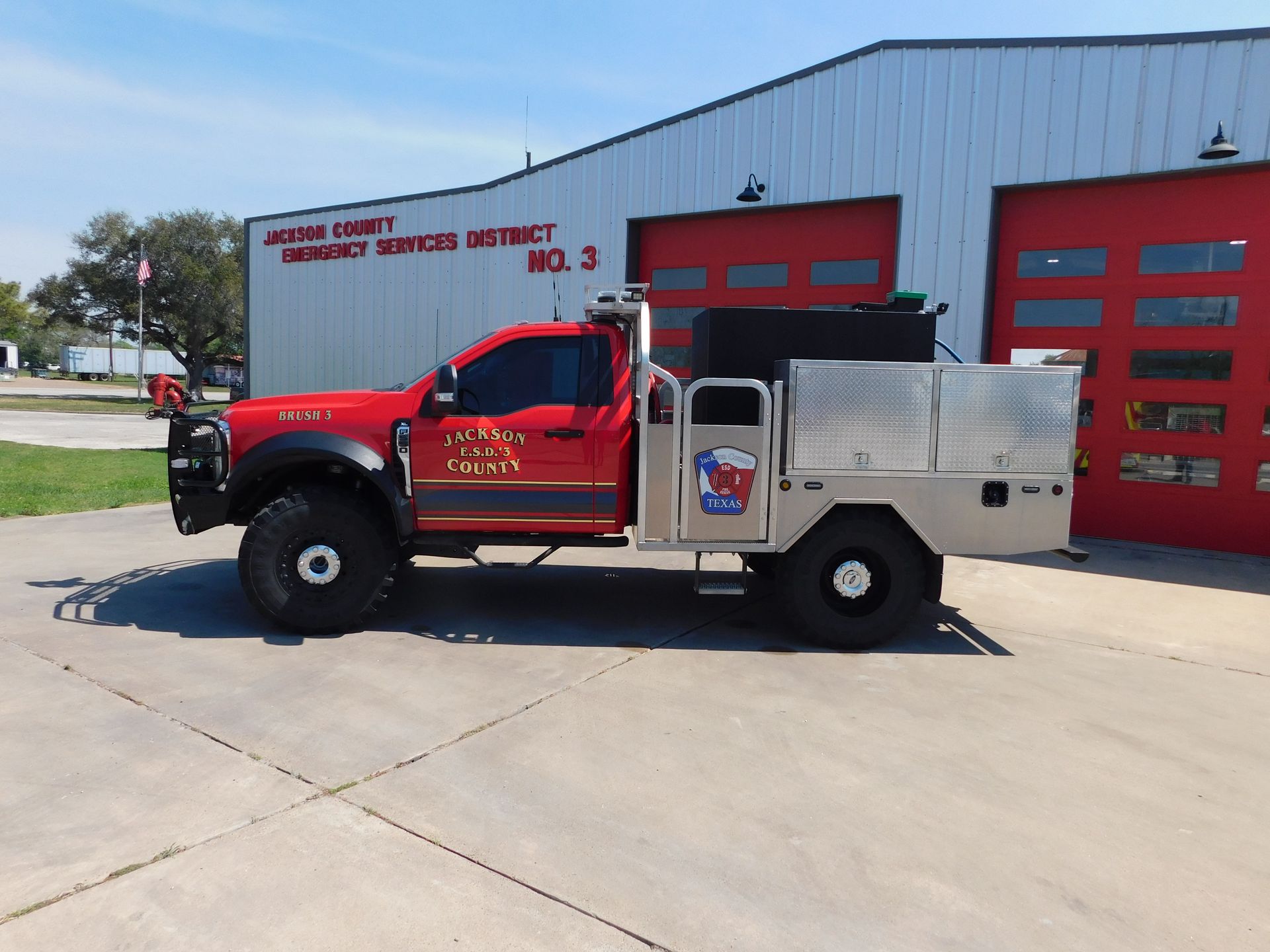 A red Jackson Fire County pickup truck with a utility bed and grill guard parked in front of a fire station.