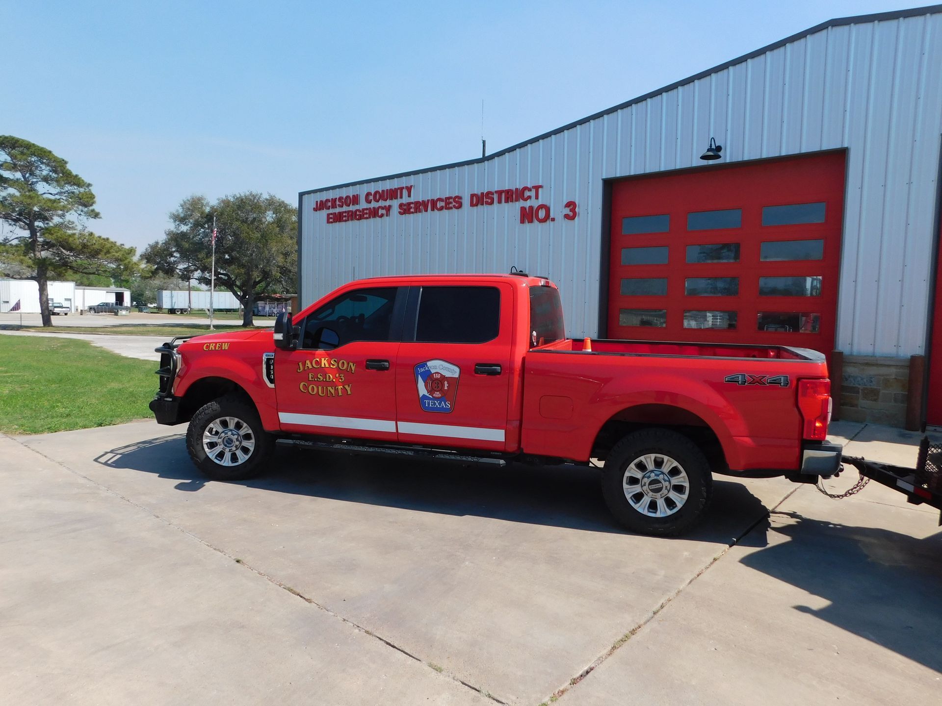 A red Jackson Fire County pickup truck with a utility bed and grill guard parked in front of a fire station.