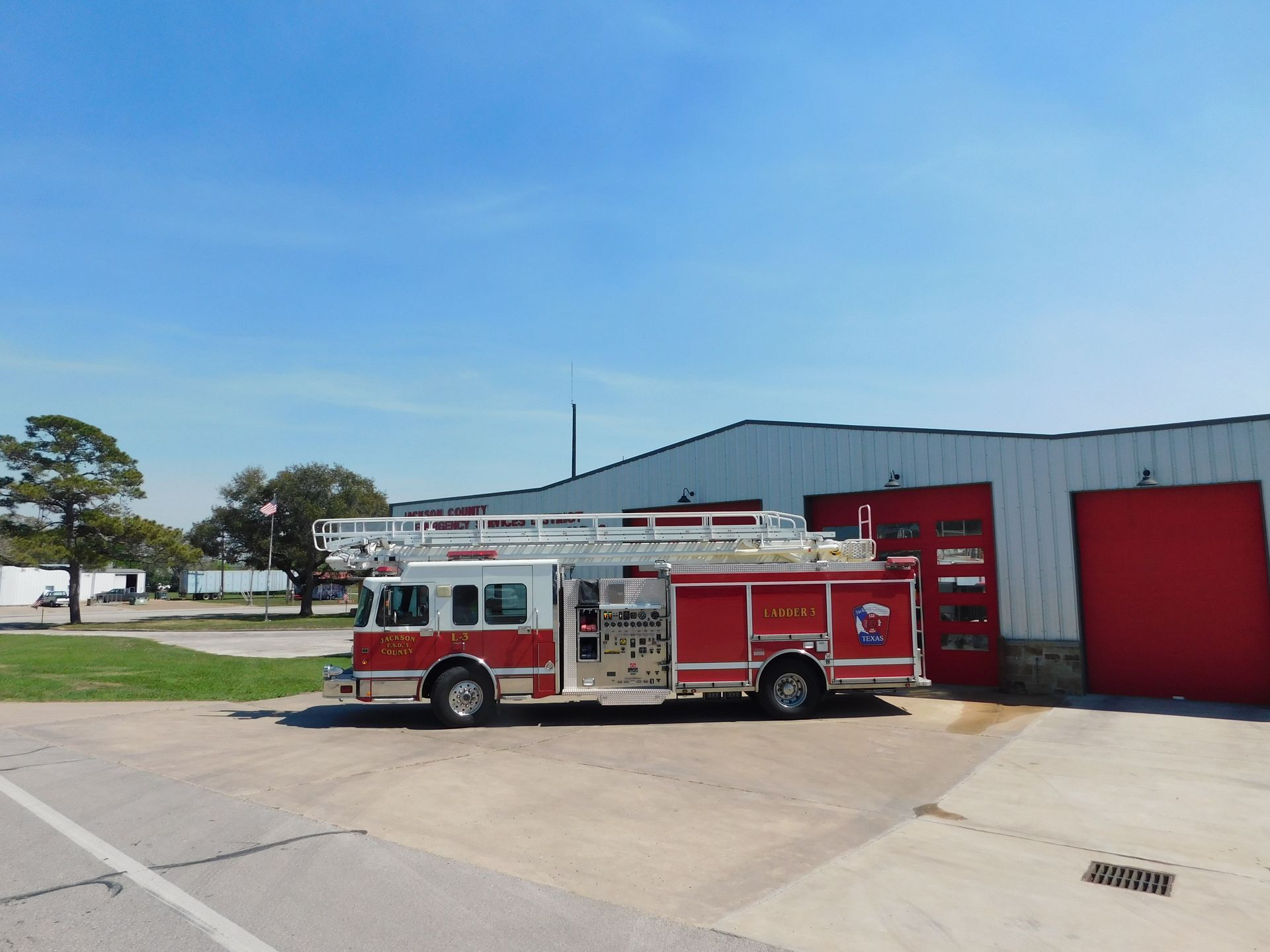 A red Jackson Fire County pickup truck with a utility bed and grill guard parked in front of a fire station.