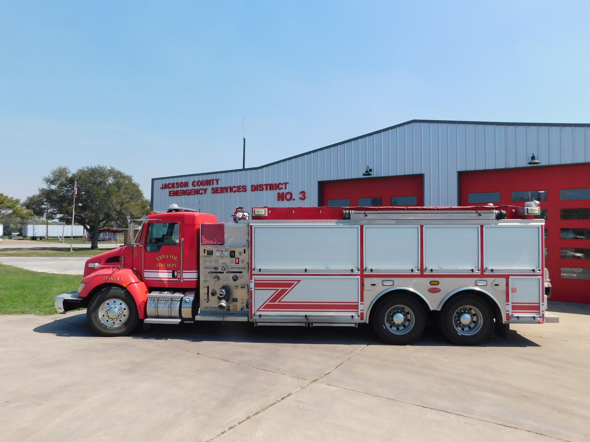 A red and silver fire truck parked on a concrete lot in front of an open garage.