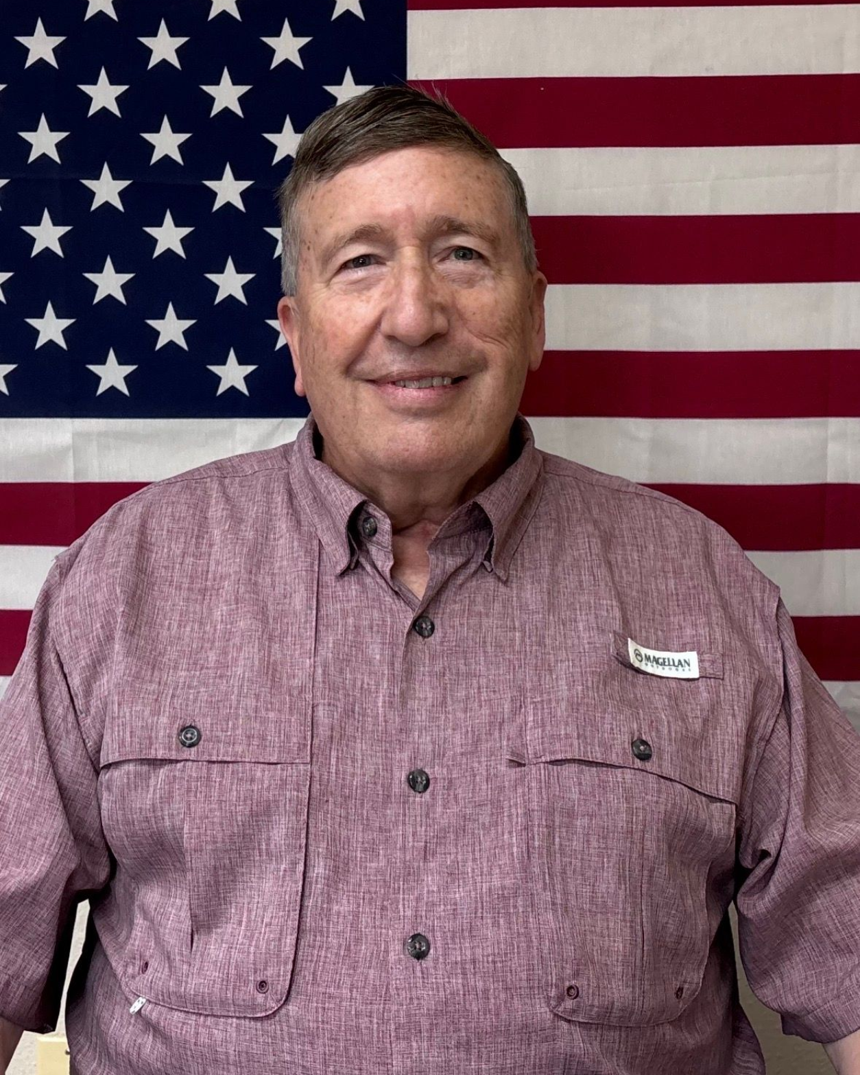 A man wearing a Jackson County Fire District 3 Commissioner polo shirt, standing in front of an American flag.
