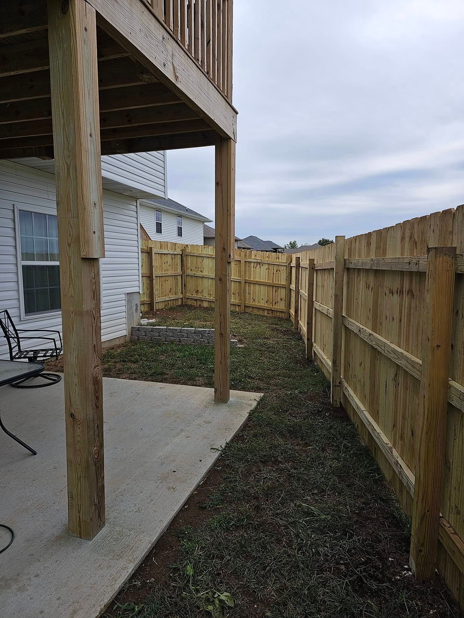 Backyard patio beside a wooden fence, with a covered porch and narrow gravel path.