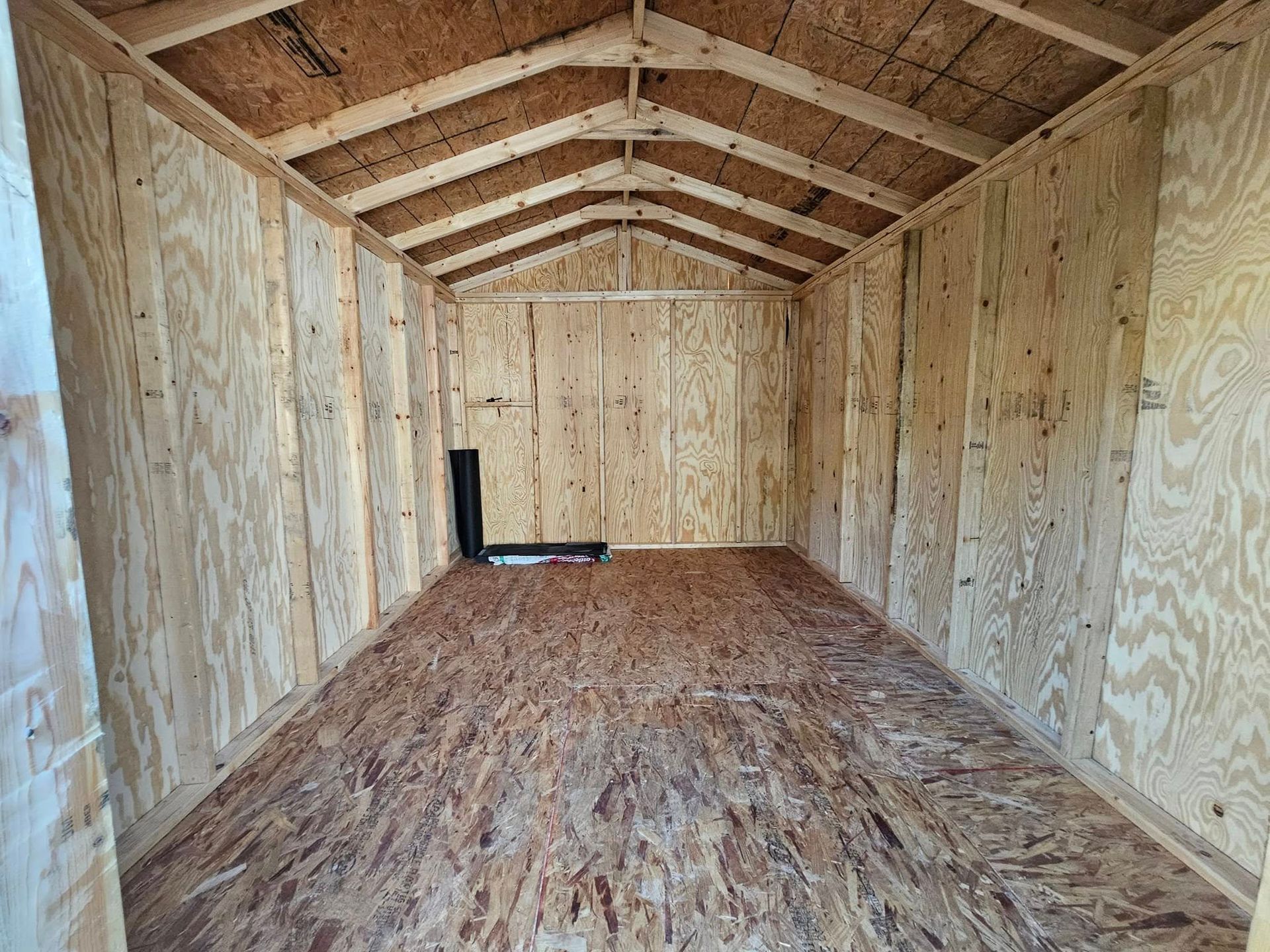 Empty plywood shed interior with wood floor and pitched ceiling