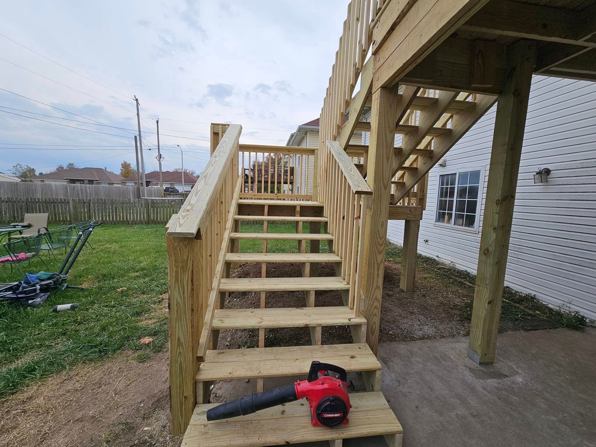 Wooden backyard stairs leading to a deck, with a red leaf blower on the steps.