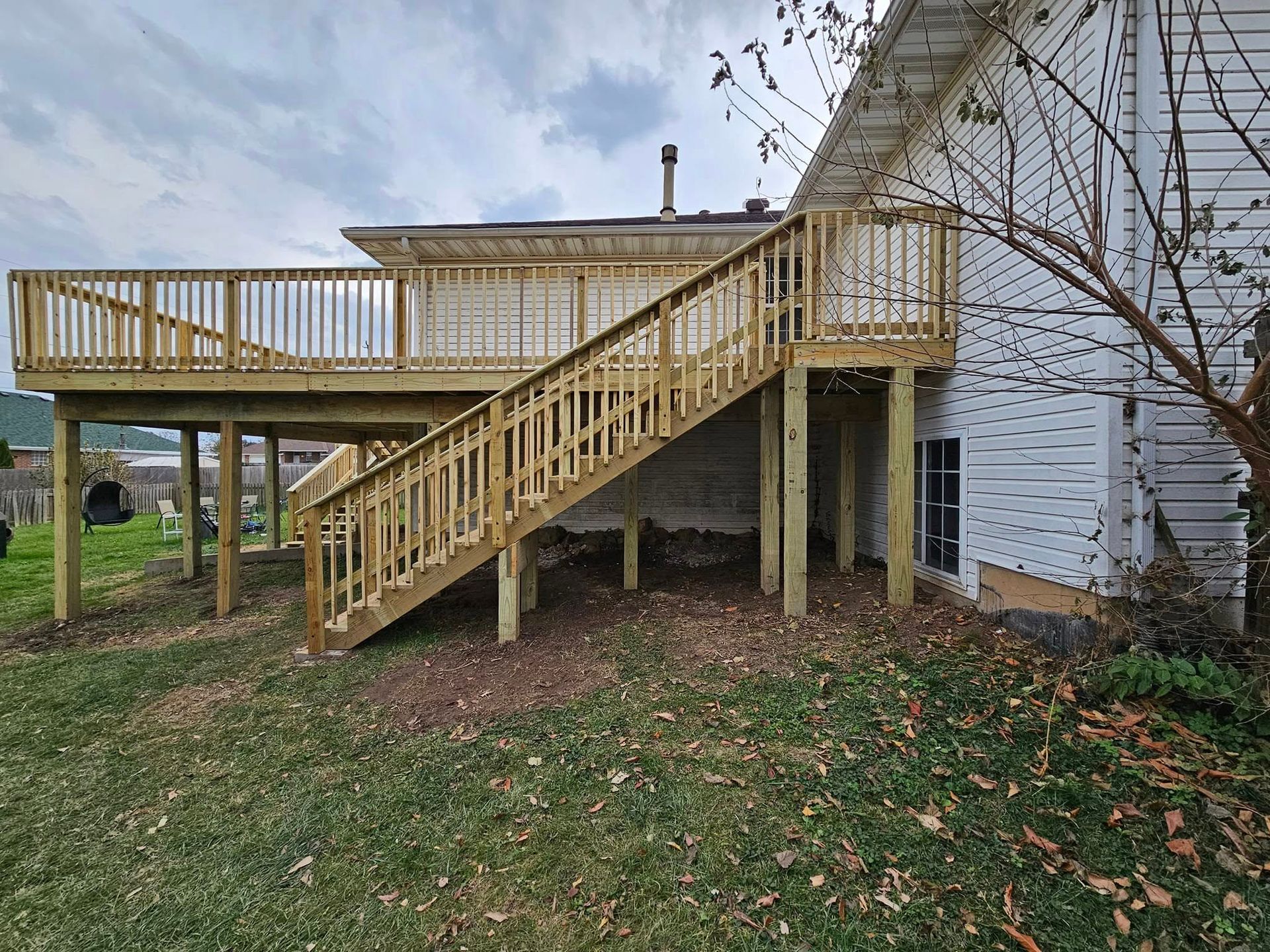 Wooden backyard deck with stairs and railing beside a house on a cloudy day