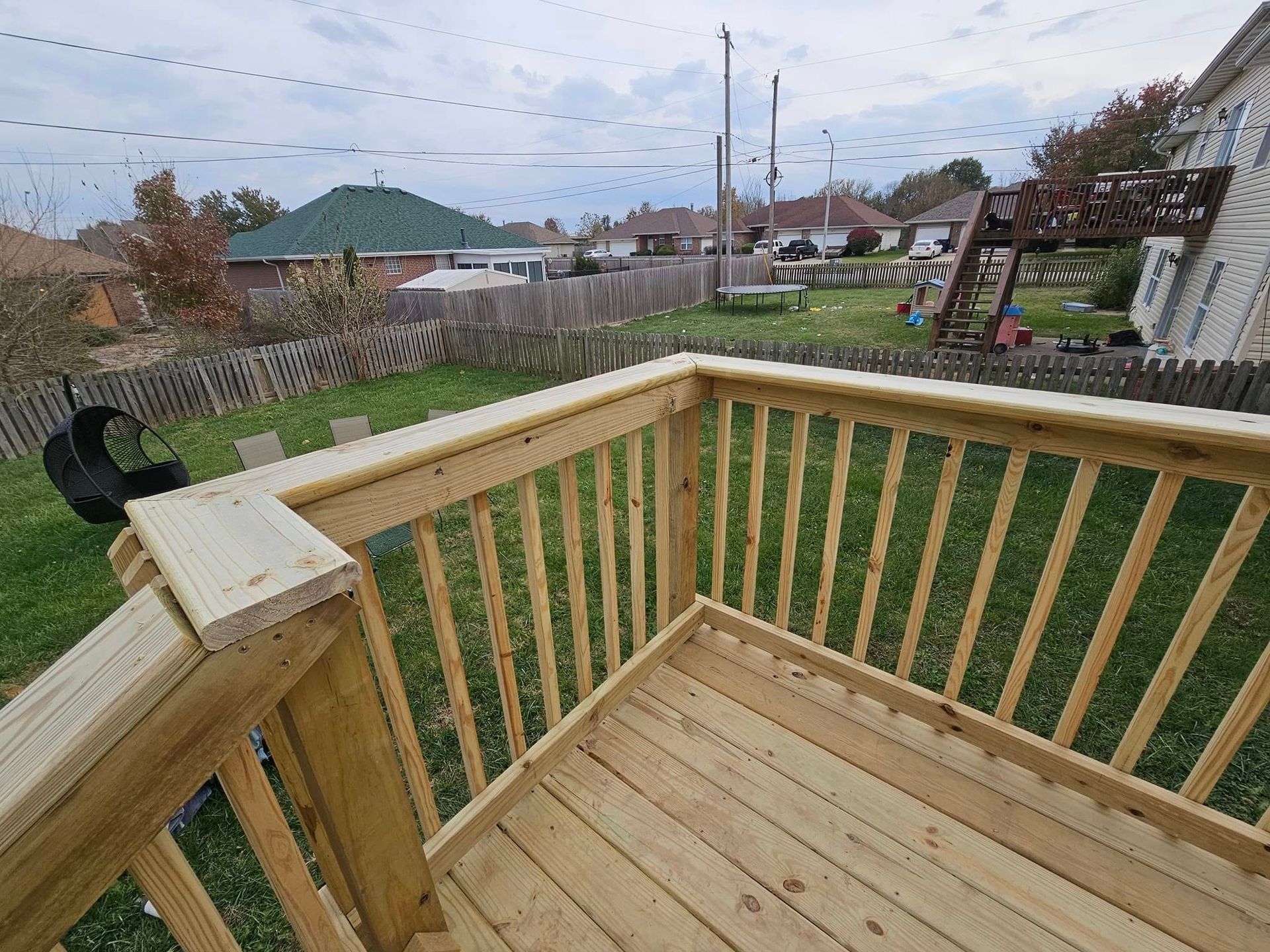 Wooden backyard deck with railing overlooking a grassy yard and neighboring houses under a cloudy sky