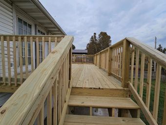 Wooden wheelchair ramp with railings leading to a house entrance, seen from the lower steps