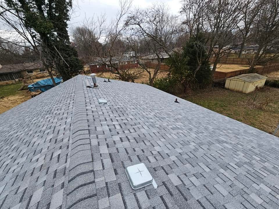 Gray shingle roof with vents in a yard with leafless trees and a shed nearby