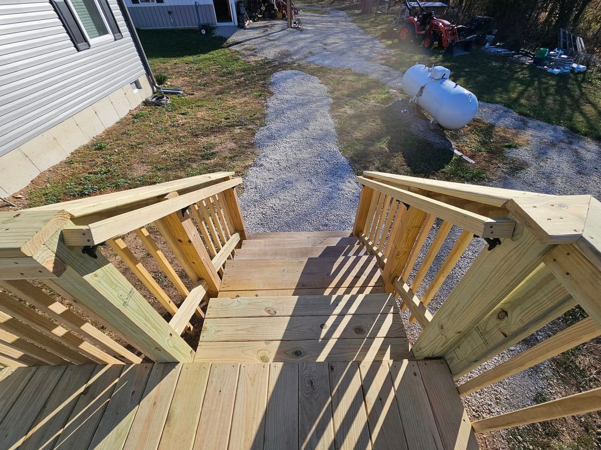 Wooden deck stairs with railings leading down to a gravel path beside a house.