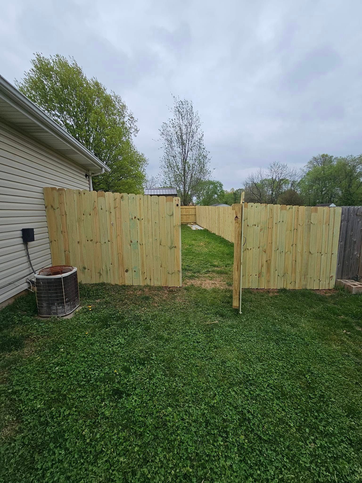 Backyard with a partially built wooden fence and a central gate opening beside a house.