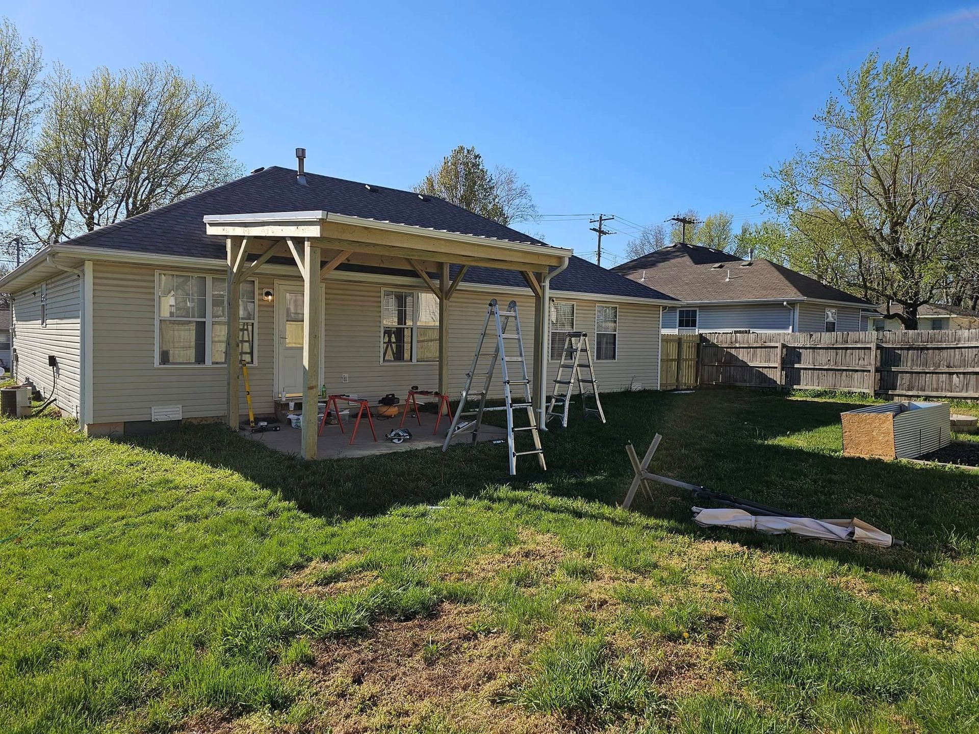 Backyard with a beige house, covered porch, and green lawn under a clear blue sky