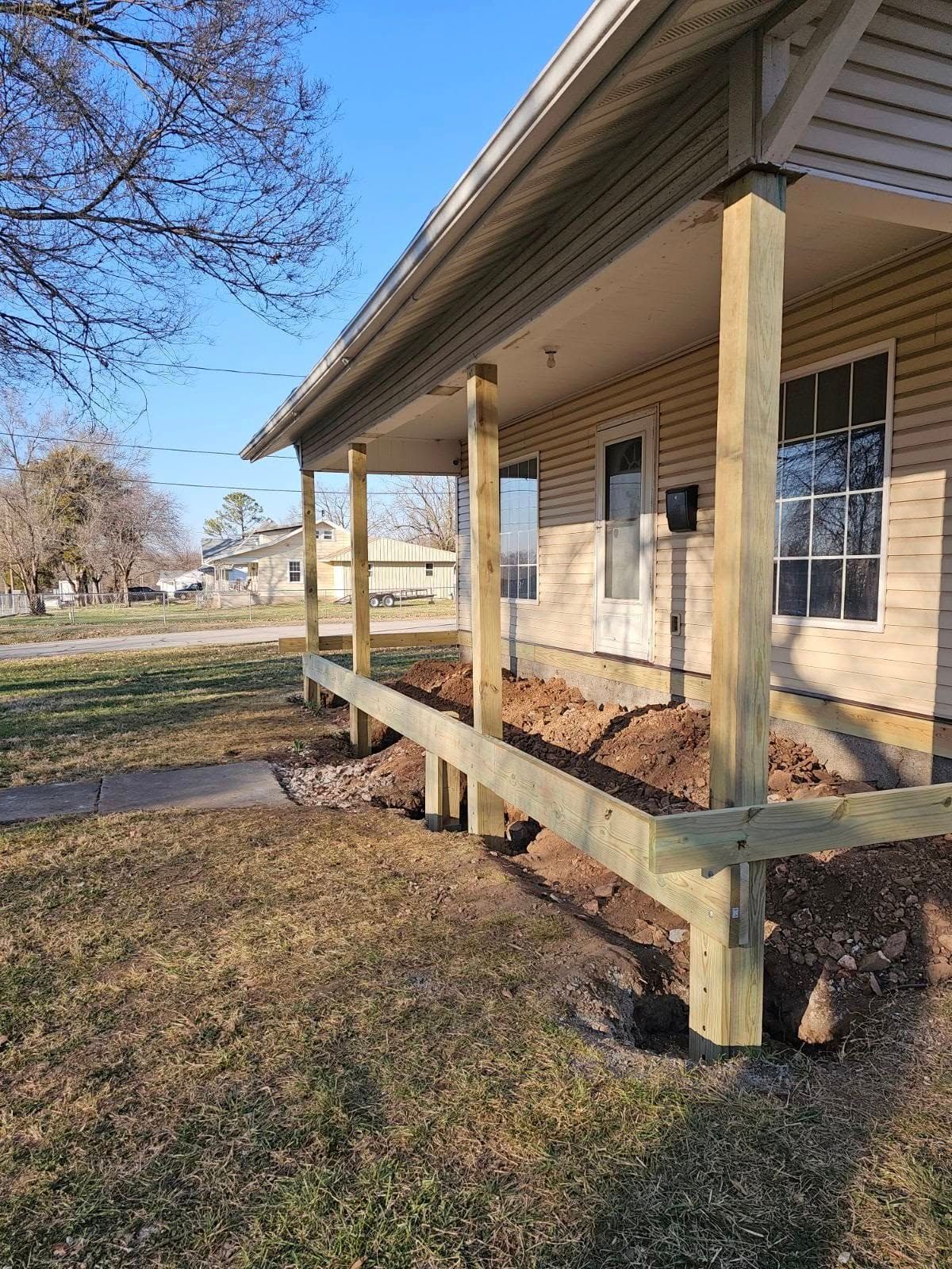 Old tan house porch with wooden ramp and columns in a grassy yard