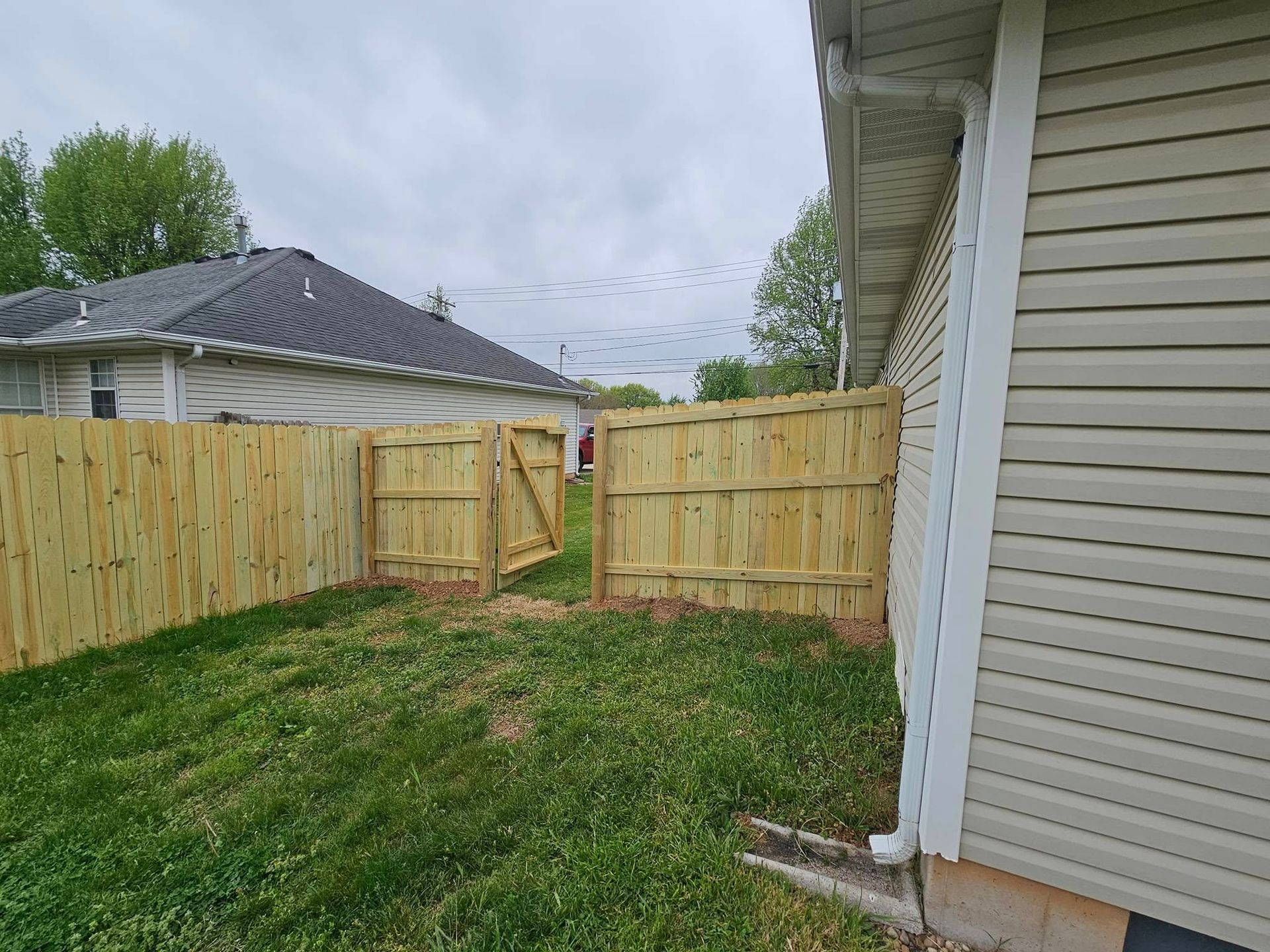 Backyard with new wooden fence and gate beside a house, under a cloudy sky