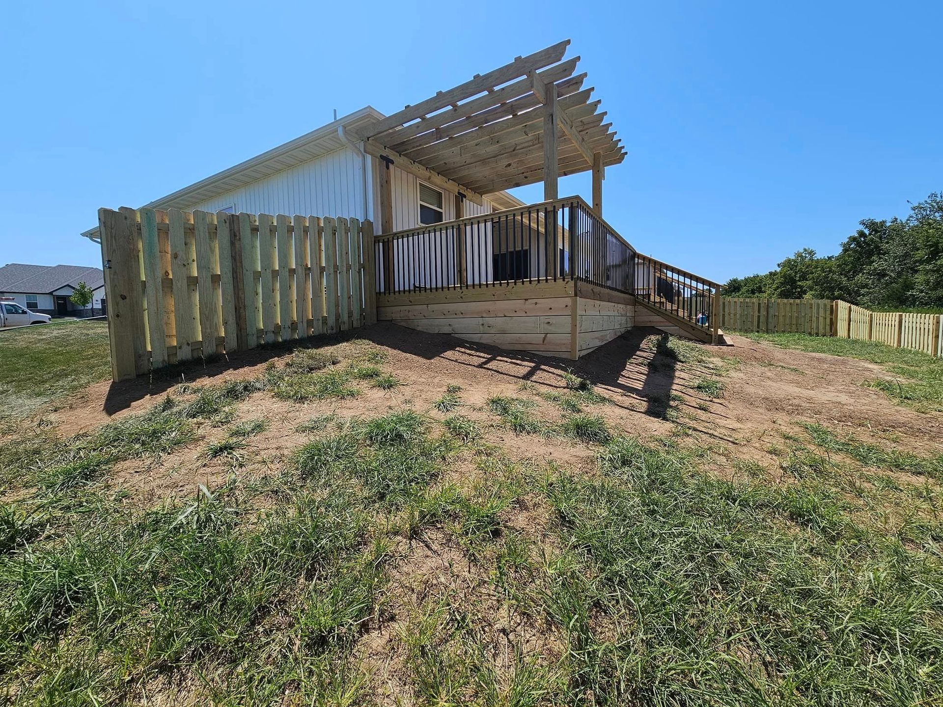 Wooden deck under construction beside a house on a sunny, grassy slope