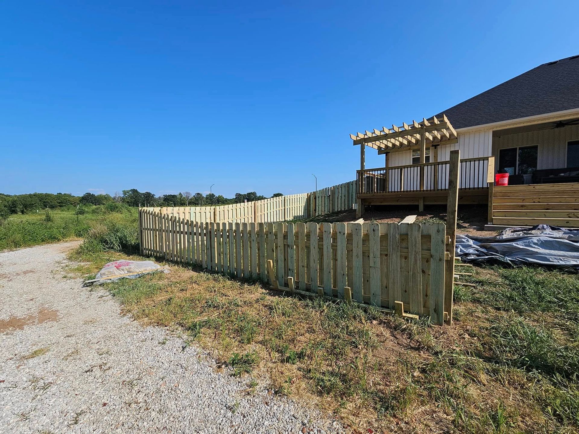Wooden fence beside a house under construction along a gravel path on a sunny day