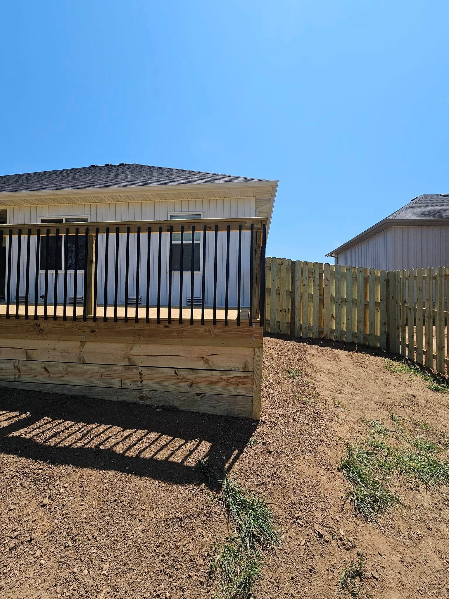 Small fenced yard with a shaded porch, gravel ground, and a clear blue sky.
