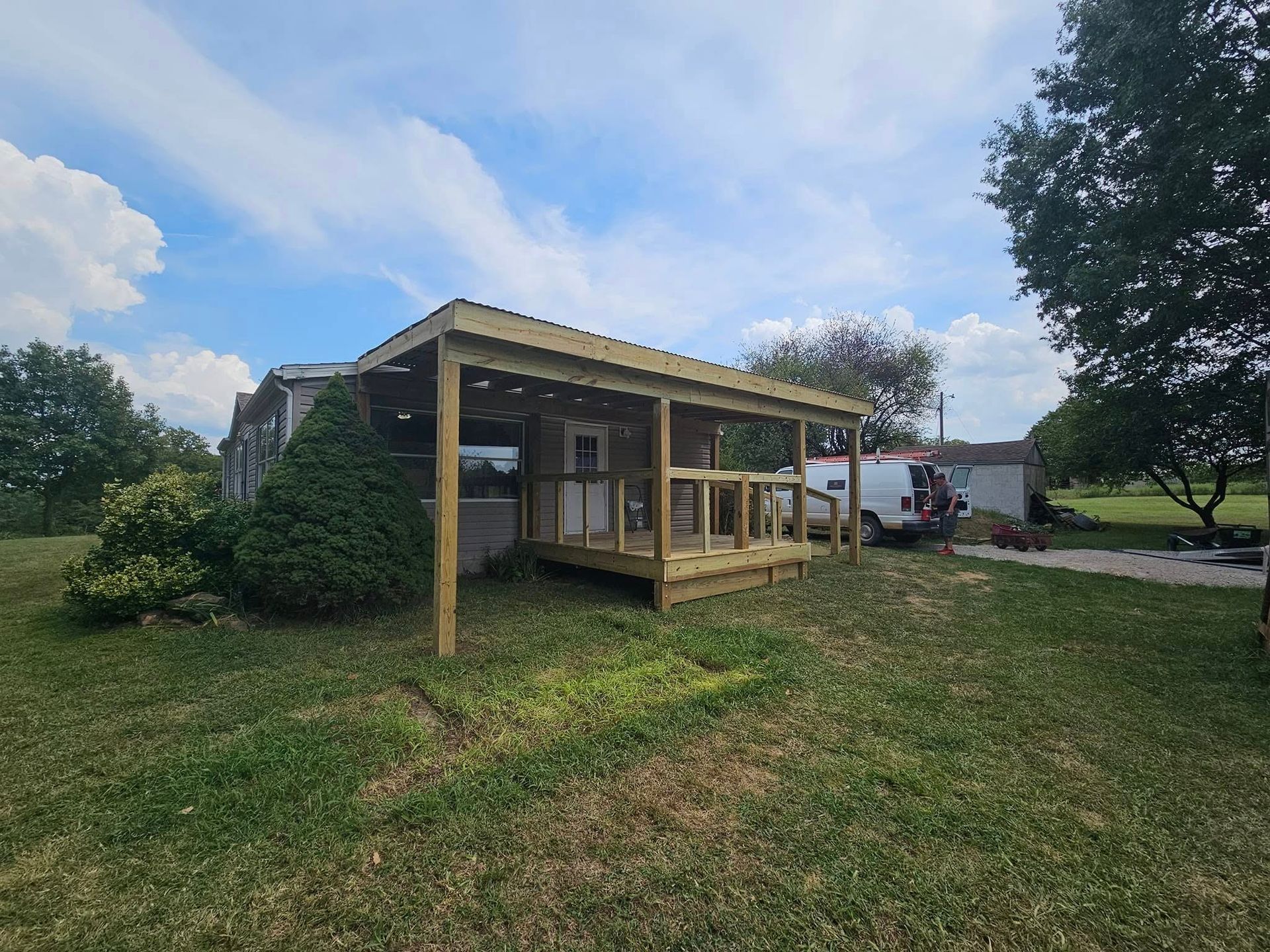 Small wooden porch shed with a slanted roof in a grassy yard under a partly cloudy sky