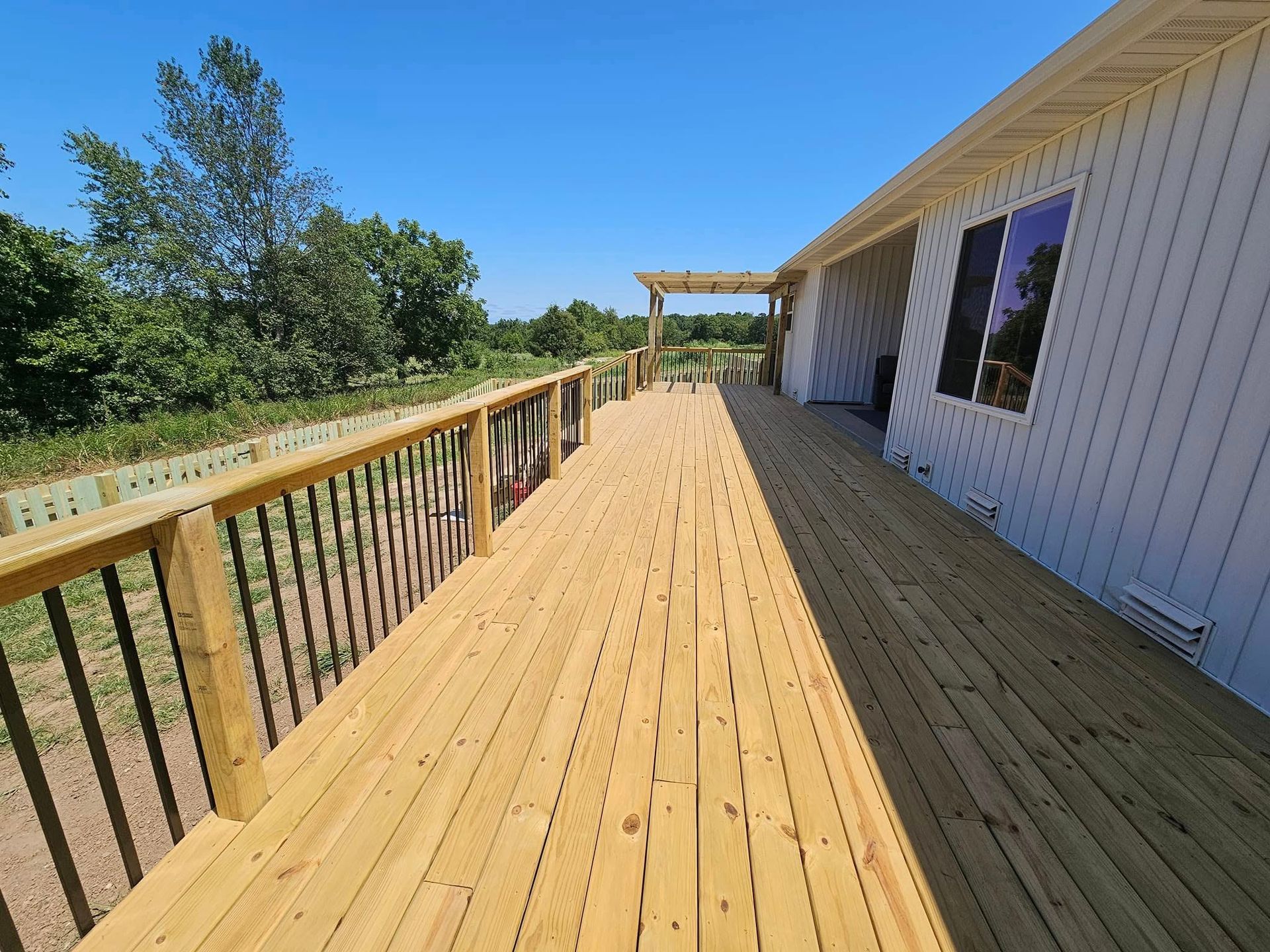 Wooden deck beside a white house, overlooking a green yard and trees on a sunny day