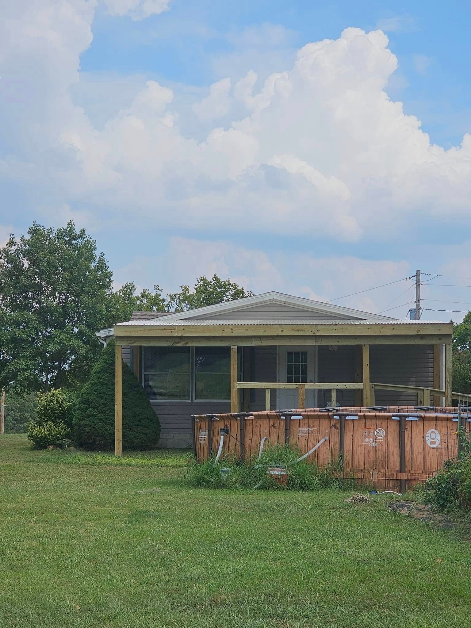 Small house with a front porch and rusty fence, set in a grassy yard under a cloudy sky.