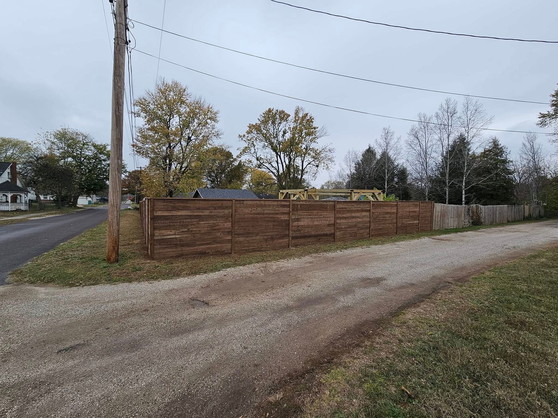 Gravel driveway beside a wooden fence and utility pole in a rural roadside setting.