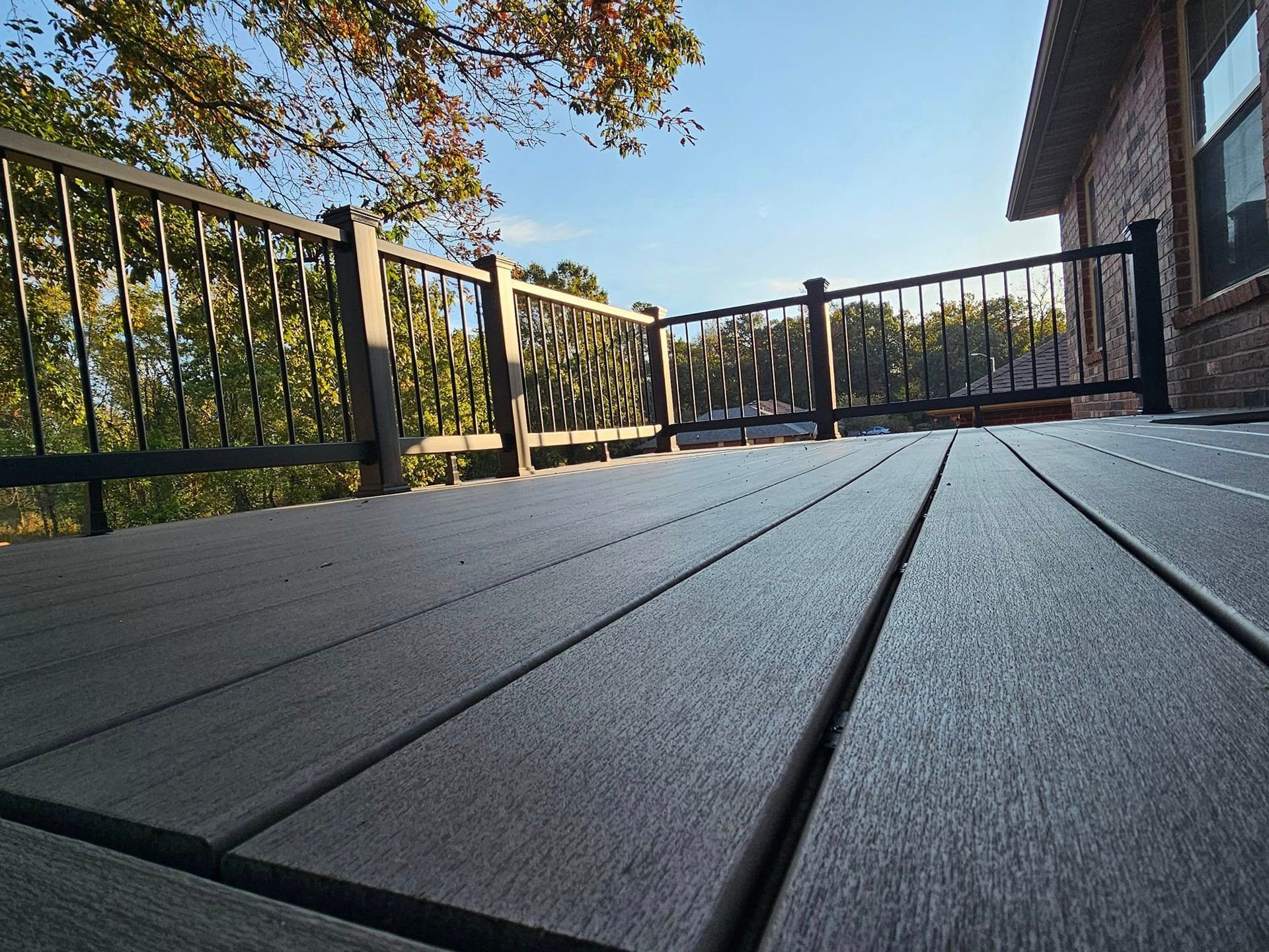 Wooden deck with black railings overlooking trees under a clear blue sky