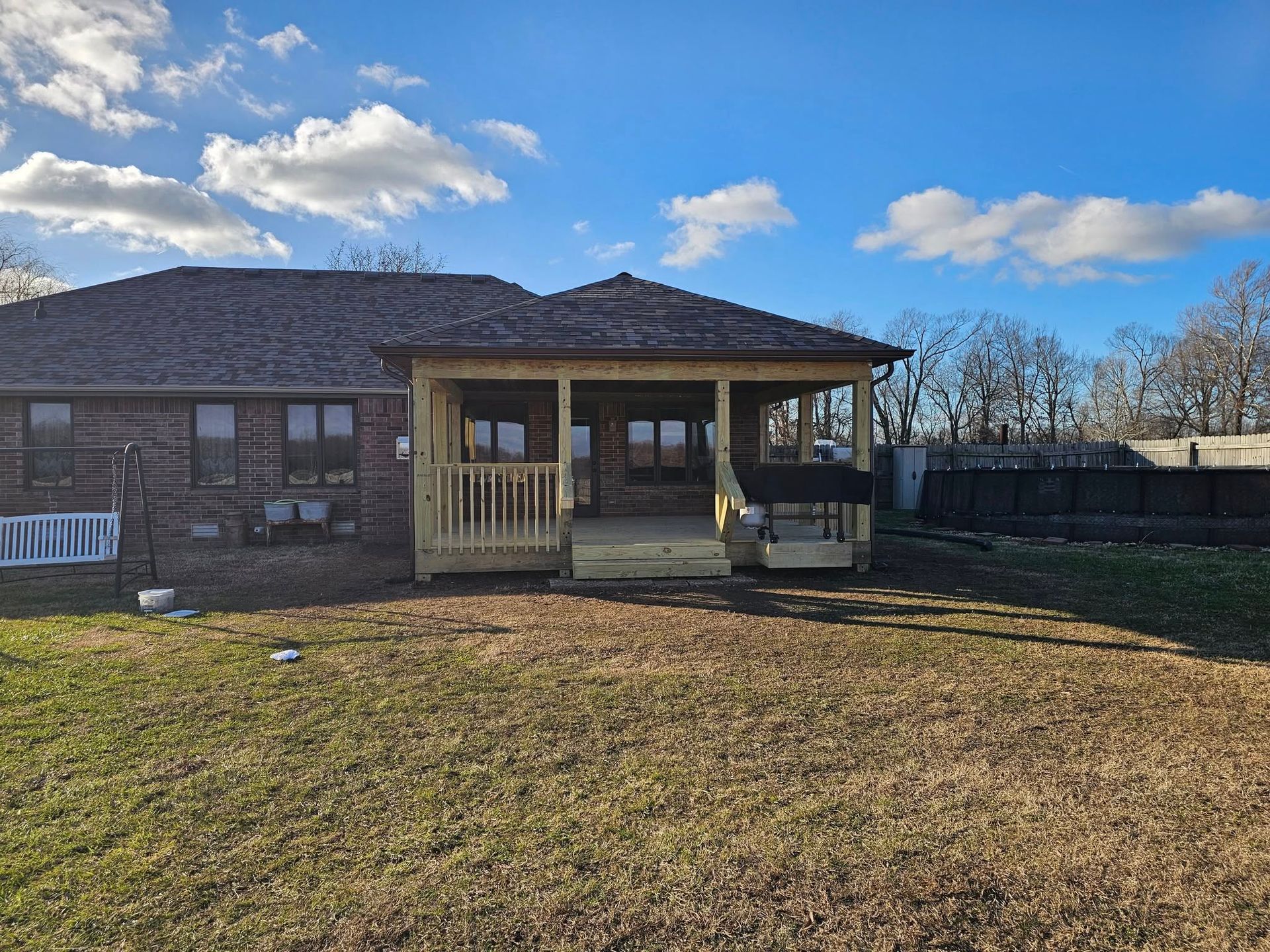 Single-story brick house with a covered porch and fenced yard under a partly cloudy sky