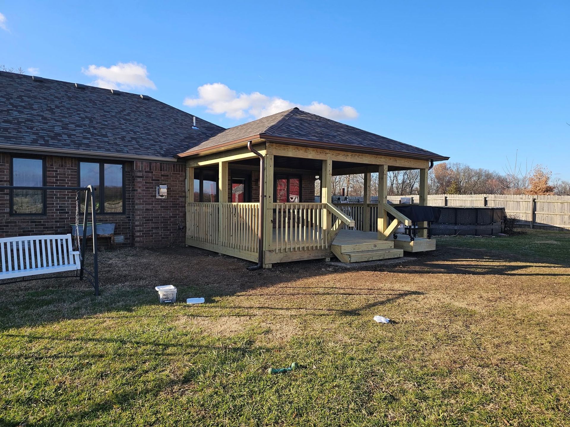Brick house with a covered porch and rocking chairs in a grassy yard under a blue sky