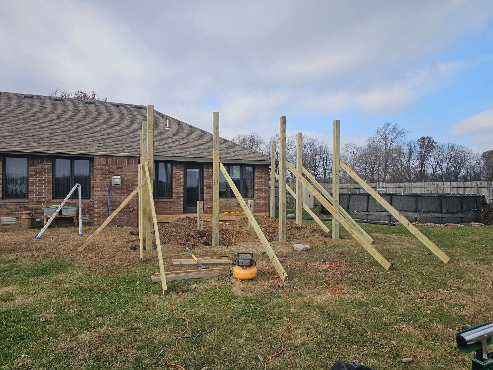 Wooden fence posts under construction in a grassy yard beside a brick house