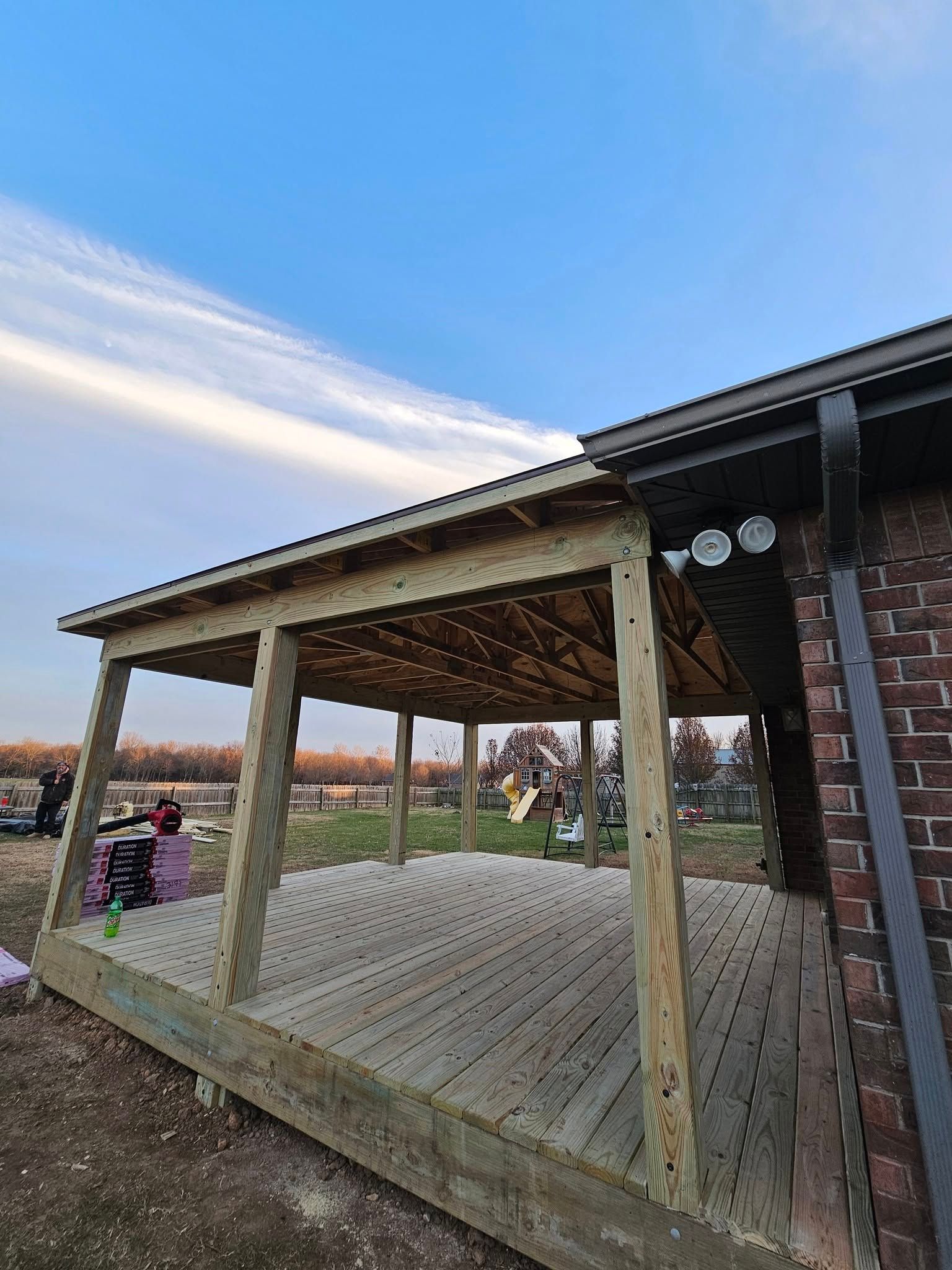 Wooden backyard deck with roofed pergola beside a brick house at sunset