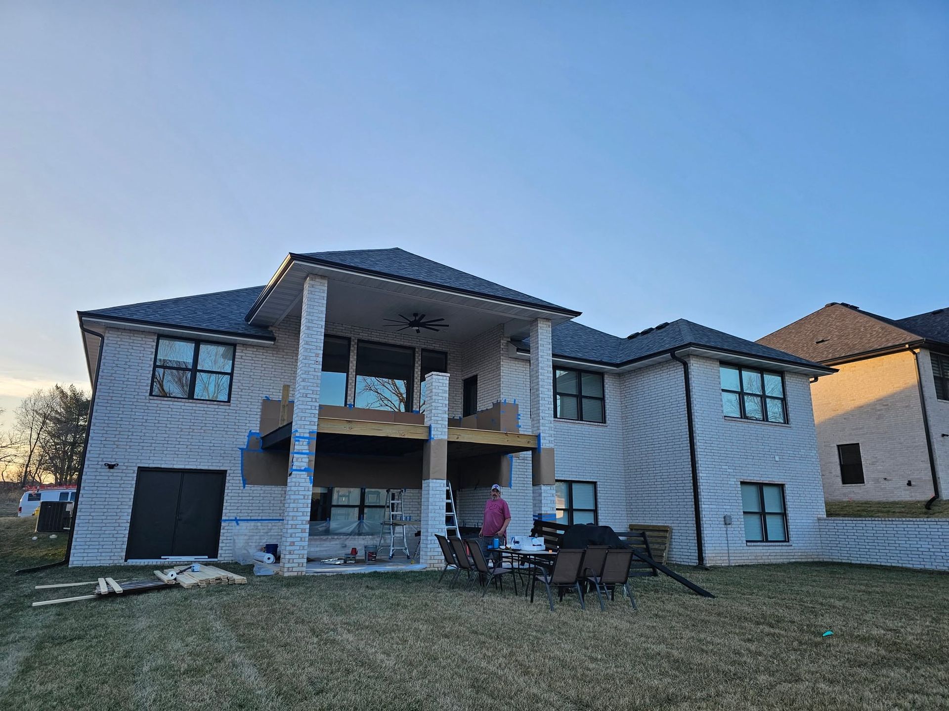 Large two-story house under construction with a porch, unfinished exterior, and a person in a pink jacket outside.