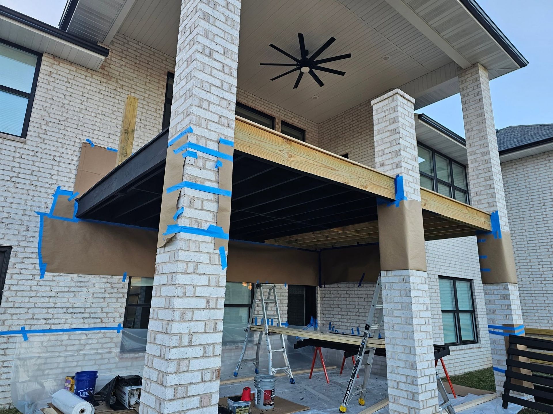 Partially built brick house with wooden porch framing and blue protective tape on exterior columns