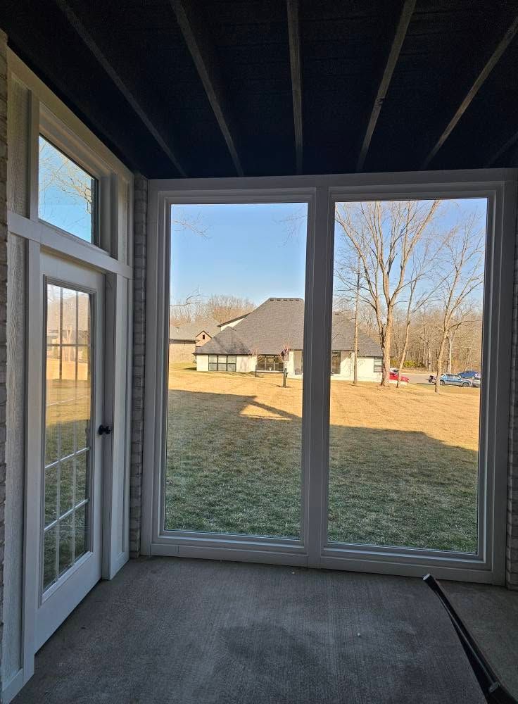 Sunroom with sliding glass doors overlooking a grassy backyard and a house in the distance