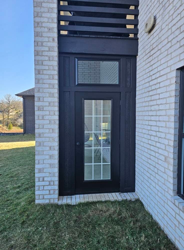 Narrow dark door in a white brick wall with a small window above and grass below