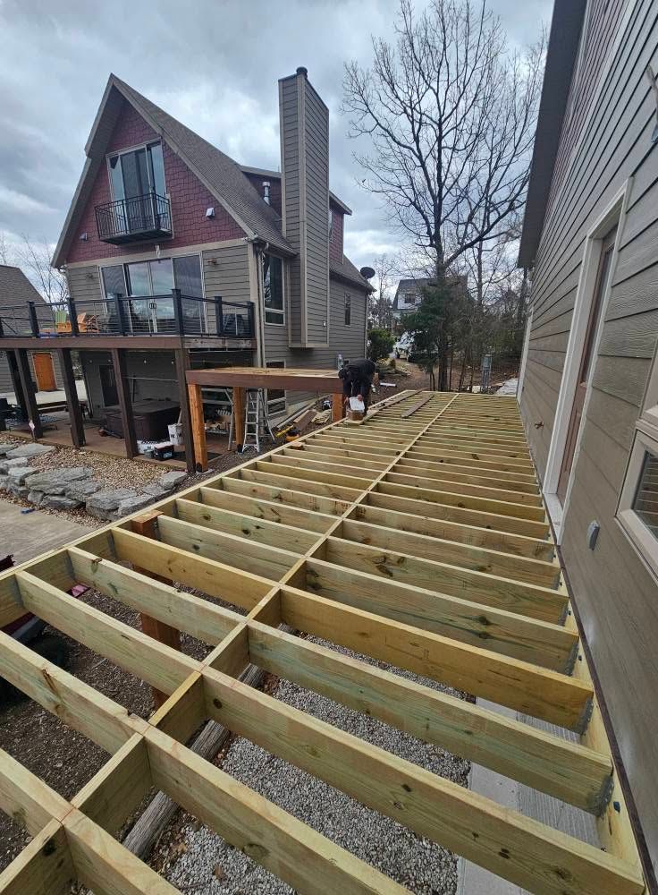 Wooden deck framing under construction beside a house with workers in the yard