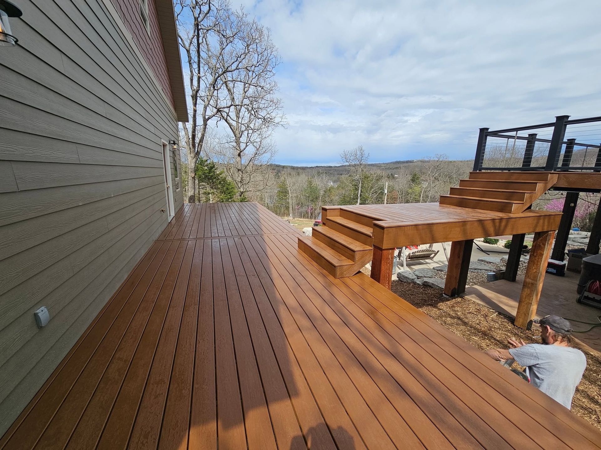 Wooden deck with railings and stairs overlooking a fenced yard on a sunny day