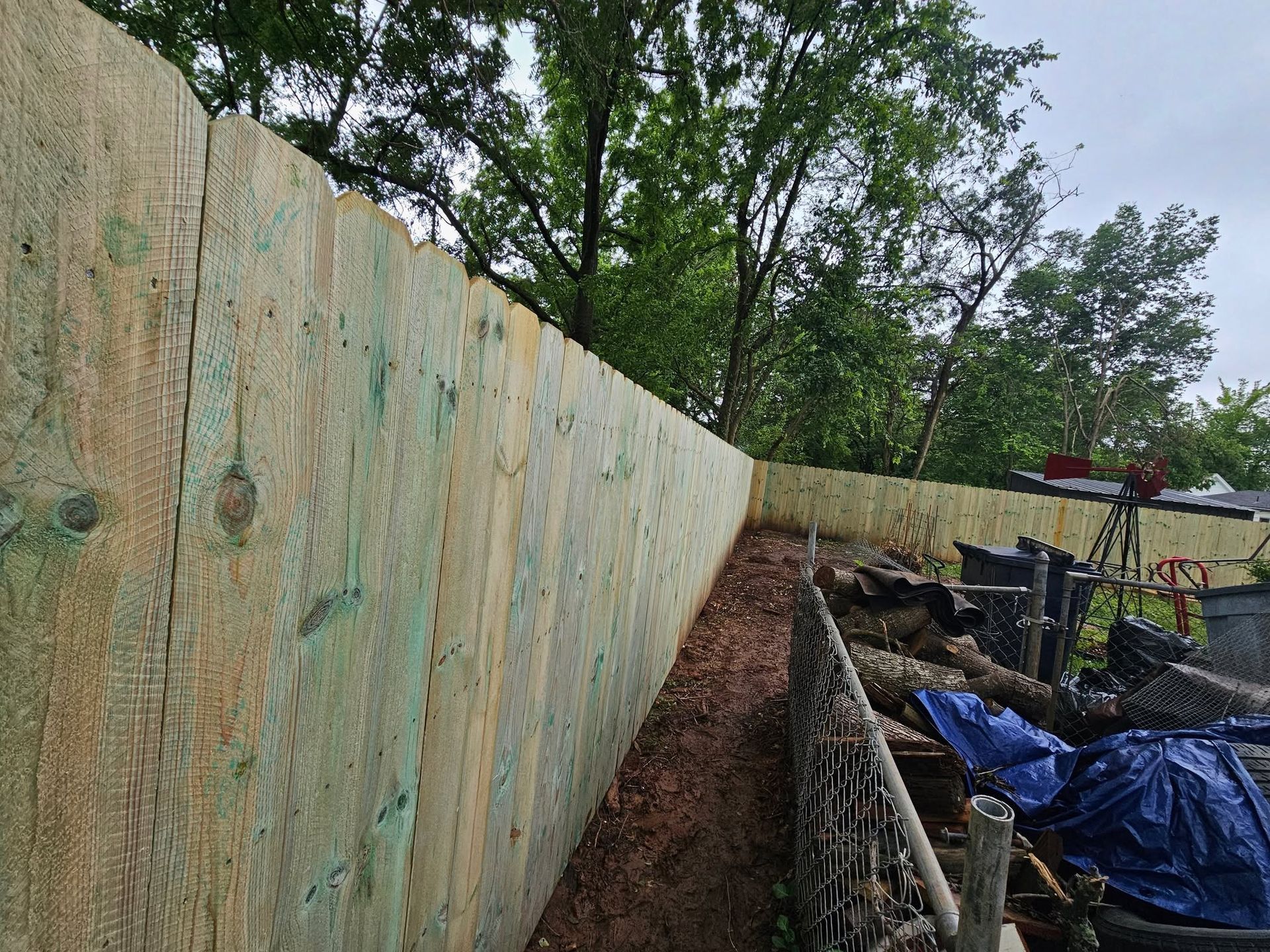 Wooden retaining wall along a dirt trench, with trees and construction materials beside it.