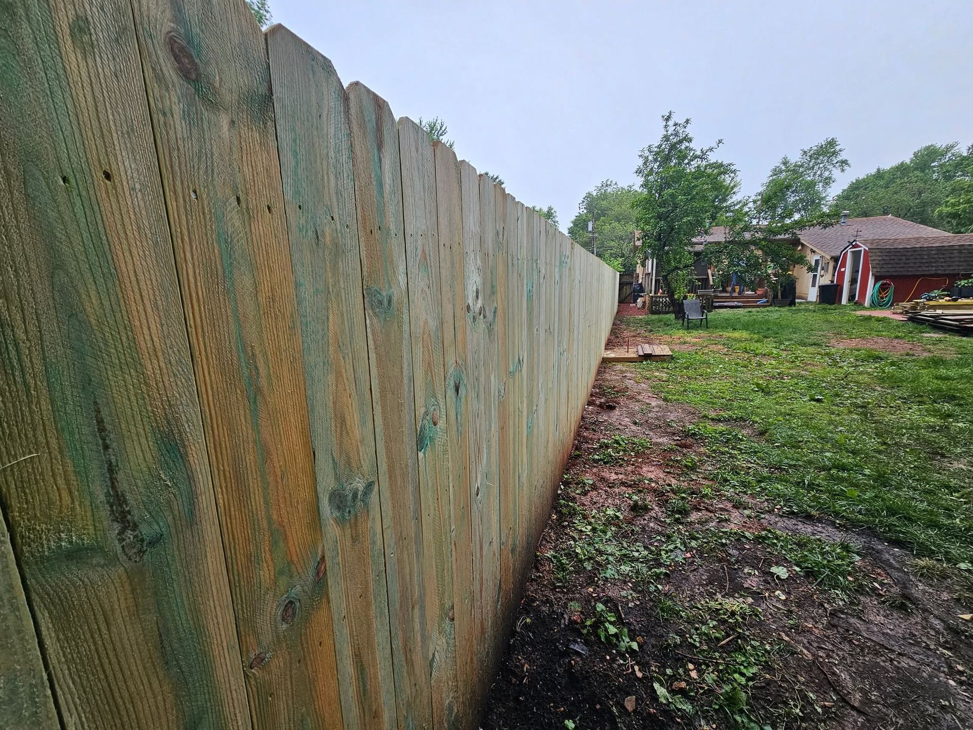 Weathered wooden fence along a grassy yard with a house and trees in the background