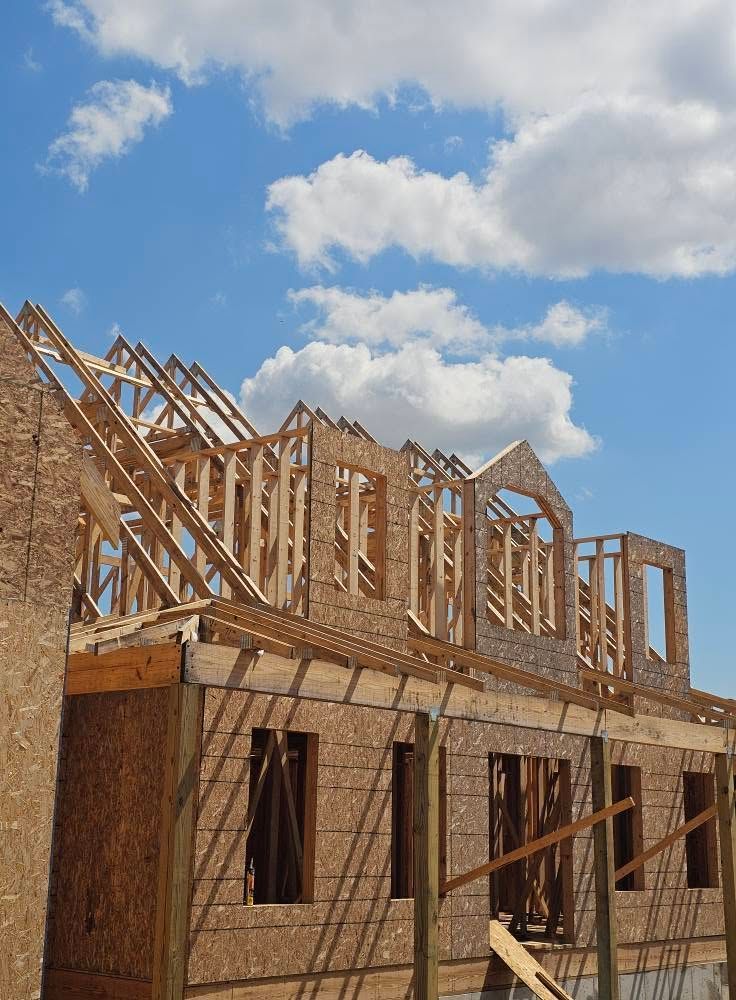 Partially built wooden house frame under a blue sky with clouds