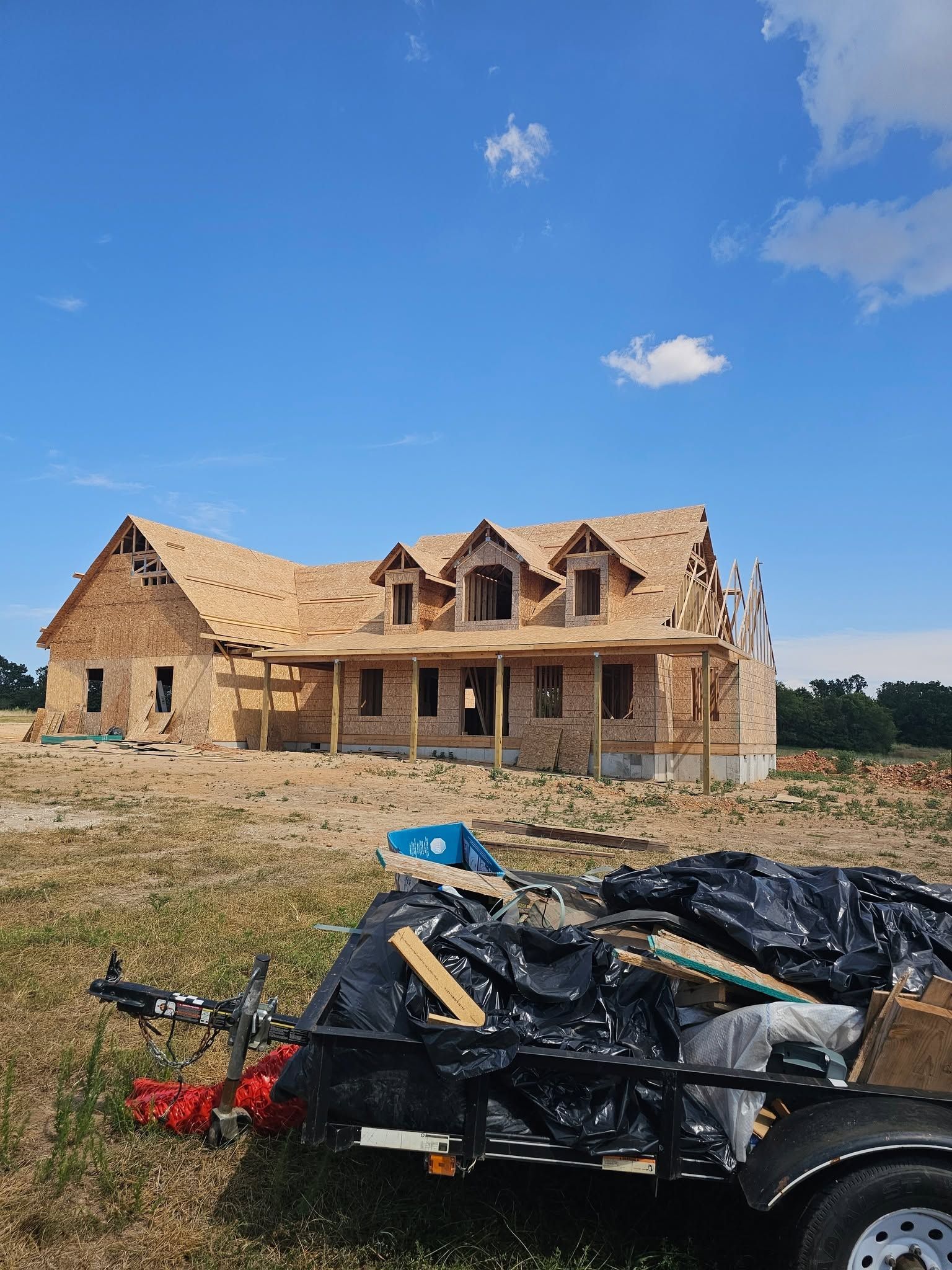 Partially built stone house under a blue sky, with a pile of construction debris in the foreground.