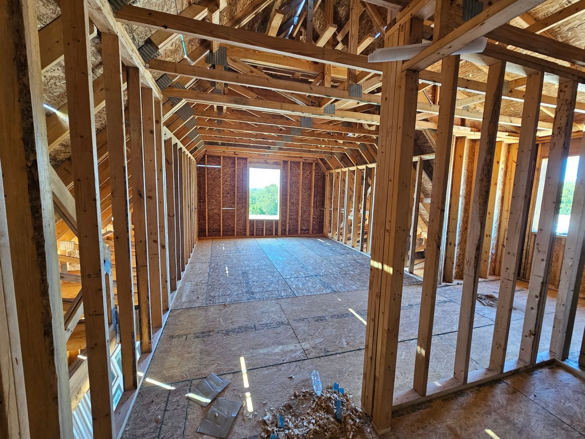 Wood-framed house interior under construction, with exposed studs, roof trusses, and subfloor.